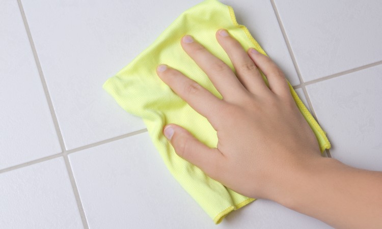 Hand with rag cleaning tile wall