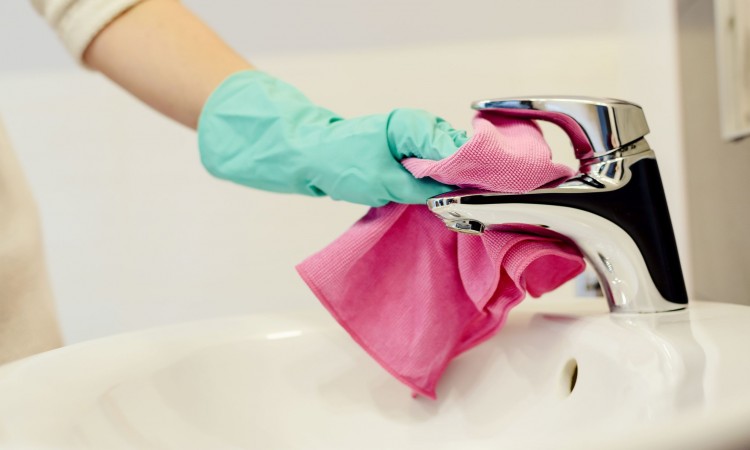 Female hands with green rubber protective gloves cleaning tap